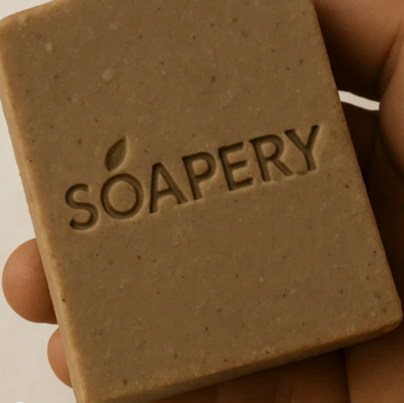 Bar of soap with 'SOAPERY' branding held in a hand against a neutral background